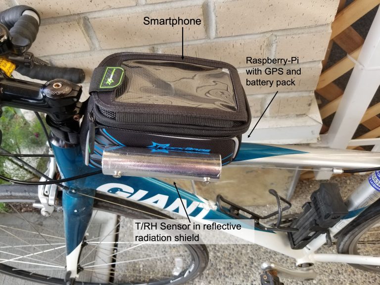 Image of a bicycle showing how a Meteobike kit is attached. The kit is mounted on the crossbar in a black pack containing the Raspberry Pi with GPS and battery pack, a T/RH sensor in a reflective radiation shield and a pouch to store a smartphone.